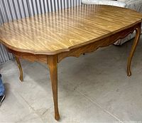 Side angle view of a wooden dining table with cabriole legs and scalloped apron in natural wood grain finish.