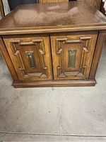 Front view showing decorative geometric wood panel doors and metal pull handles on liquor cabinet.