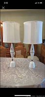 Front view of both tall cream colored MCM side table lamps with cylindrical shades on a patterned tablecloth.