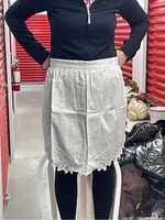 White handmade waist apron with lace edging and a single pocket amid a mostly black outfit background.