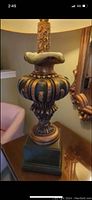 Front angle view of the ornate ceramic table lamp showing detailed ribbed and carved mid-section, square base, and the corded lamp stem portion.