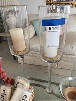 Two tall clear glass candle holders with white pillar candles and decorative beads inside, placed on a glass table.