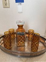 Photo of decanter with stopper, six matching glasses, and silver tray on carpeted floor showing overall contents of the set.