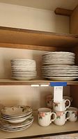 Cabinet shelf with stacks of Mikasa Country Classics Fruit Panorama plates and mugs