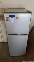 Front view of small white refrigerator with freezer on top, worn and with stickers on door.