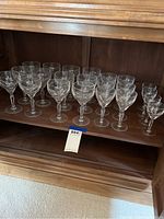 22 pieces of clear glass stemware arranged on a wooden shelf, mixed sizes of wine and cocktail glasses visible.