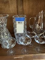 Etched glass vases, pitchers, and five champagne glasses displayed on wood shelf