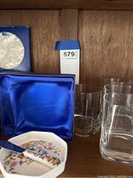 Highball glasses positioned upright alongside an octagonal floral cheese dish with matching spreading knife in front, some items partially boxed.