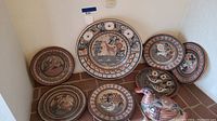 Six Mexican pottery pieces displayed on a tiled floor corner, including five hand-painted decorative plates and one bird figurine.