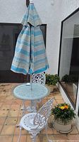 Full view of the outdoor patio set showing white metal table, two matching chairs, and closed striped umbrella in the center.