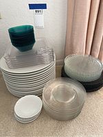Stack of various plates including white ceramic, clear glass, black and green tinted square plates, and small white plates.