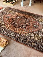 Photo of a larger oriental style rug with rust, brown, cream, and black colors in a central medallion and floral pattern.