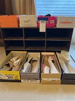 Eight pairs of women's shoes in their original boxes arranged in front of a black cardboard shoe holder with multiple compartments.