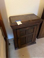 Side view of the dark walnut side table cabinet showing single paneled door and top molding detail with a label on top.