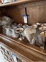 Shelf showing 14 silver goblets of two sizes, many wrapped in plastic liners.