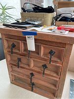 Front full view of small wooden chest with seven drawers and black strap handles.