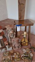 Overview showing carved wood chair, ceramic figurine, metal horse, terracotta carvings, and painted plaques