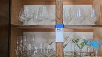 Full view of shelf with variety of clear stemware glasses including brandy snifters, martini glasses and wine glasses.