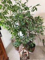 Photo showing two large artificial green trees in pots and one decorative birdhouse placed in front of one tree.