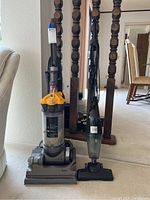 Two vacuums shown side by side: a Dyson DC33 upright vacuum and a smaller Eureka handheld vacuum, both with dust containers showing dust residue.