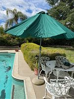 Wide view of table and chairs next to pool with open green umbrella.