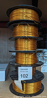 Stack of six black plastic spools wound with metallic gold filament