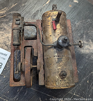 Top angled view of the brass boiler, valve, piston assembly and red base showing condition and rust.