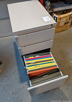 Photo showing the file cabinet with the bottom drawer open revealing colorful Pendaflex hanging file folders inside.