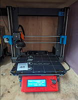 Front view of assembled Prusa i3 MK3S with textured spring steel bed loaded, control box LCD shows total filament and print time