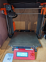 Front view of custom assembled Prusa MK3S printer showing steel frame, orange plastic brackets, glass print bed and red LCD controller