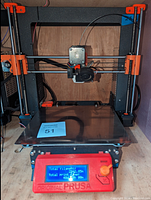 Front view of printer installed with clear glass bed plate and red Original Prusa LCD control panel displaying usage statistics