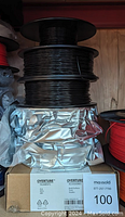 Stack of black filament spools wrapped in foil, showing labels for Overture filaments and accessories