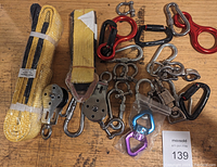 Photo showing various yellow straps, metal pulleys, metal hooks, carabiners in multiple colors and sizes arranged on a wooden surface.