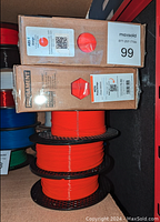 Boxed and opened spools of orange Prusament 3D printer filament. Visible three rolls stacked with filament and one box labeled ABS-T Orange.