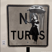 A 24x24 inch metal wall sign with black stencil art of a woman holding an umbrella, partial text 'N TURNS'. Sign has a crackled, weather-worn appearance.
