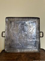 Front view of square silver-plated tray with floral engraving and two handles