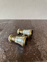 Antique small opera glasses with mother of pearl inlays and brass construction, placed on a marble surface.