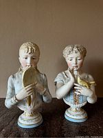 Pair of antique hand-painted gilt bisque porcelain busts on bases with gold detailing. Both are about 13 inches tall and depict young women in 18th-century style dress.