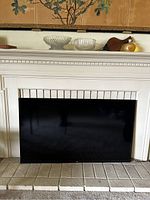 Front view of large black screen TV positioned in a fireplace area, showing the entire display and surrounding frame.