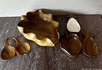Large carved leaf/flower-shaped monkey pod wood bowl with smaller pineapple and leaf-shaped bowls and two wooden utensils.