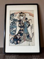 Framed print showing full figure of woman in floral kimono beside a large decorated vase.