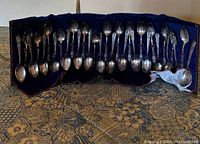 Full set of 24-25 vintage William Rogers presidential commemorative spoons displayed on blue velvet backing.