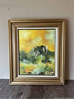 Full view of the signed oil painting in a gold frame placed against the wall on a wooden surface.