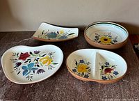 Four Stangl pottery bowls displayed on a surface, clearly showing hand-painted floral designs and earthy colored rims.