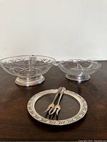 Photo showing two crystal bowls with sterling silver bases and the silver rimmed plate with two small serving forks on top, placed on wooden surface.