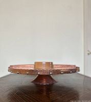 Side view showing hammered copper rim with metal studs and wooden base of lazy Susan