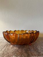 Side view of amber glass bowl showing scalloped edges and one foot visible under the bowl