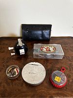 Photo showcasing entire vintage fishing gear lot on a brown surface: reel, black leather case, Corina plastic box, Leader metal box, round metal tin, and red-gray container.