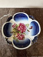 Top view of vintage decorative plate showing pink rose floral motif on blue and white scalloped background with gold accents