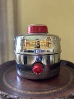 Front view of the vintage chrome Knapp Monarch Therm-a-Jug, showing red spigot and white and red cap/cup on top with label.